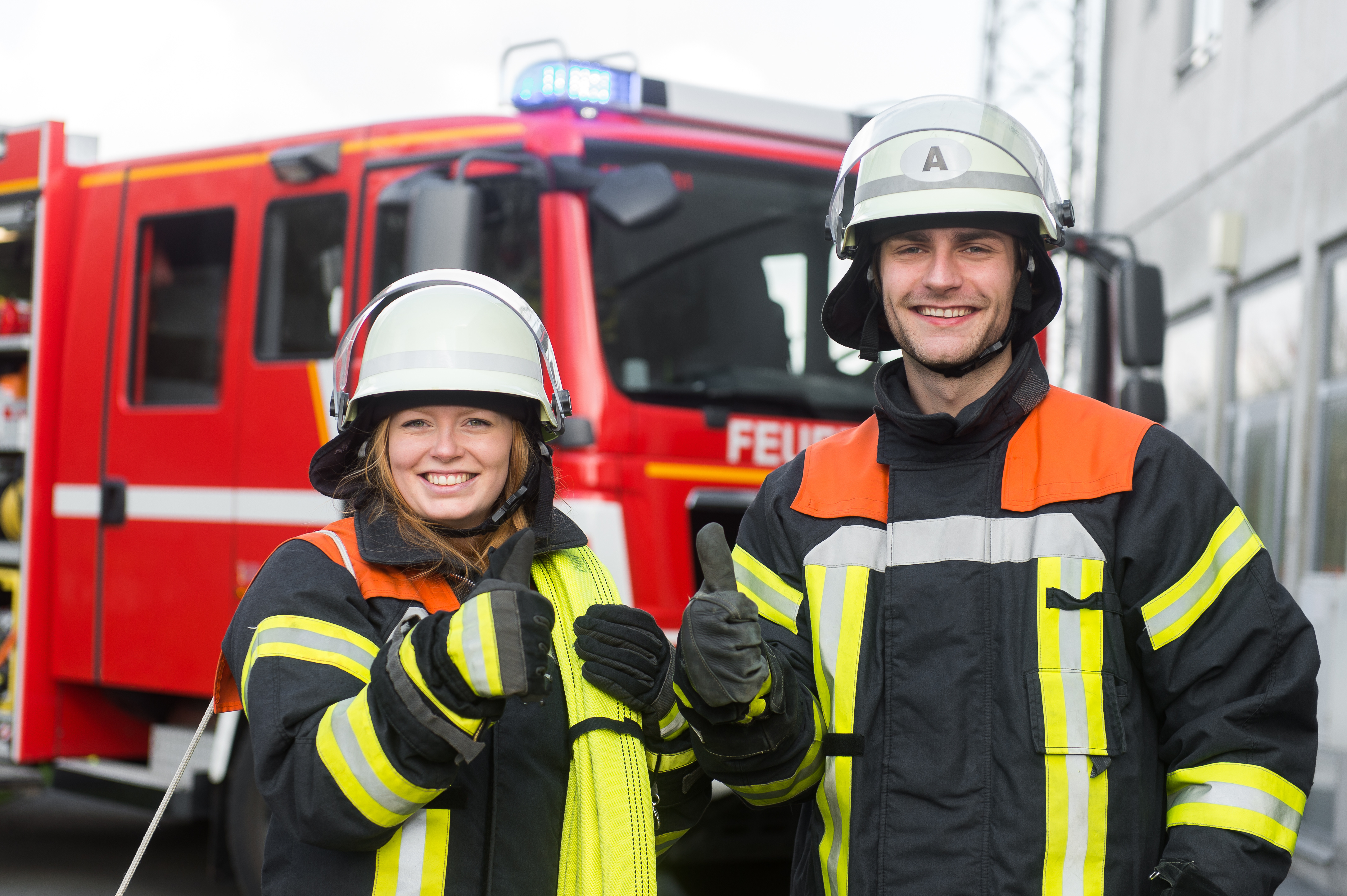 Feuerwehrmann und Feuerwehrfrau strecken den Daumen in die Kamera Feuerwehrmann und Feuerwehrfrau strecken den Daumen in die Kamera