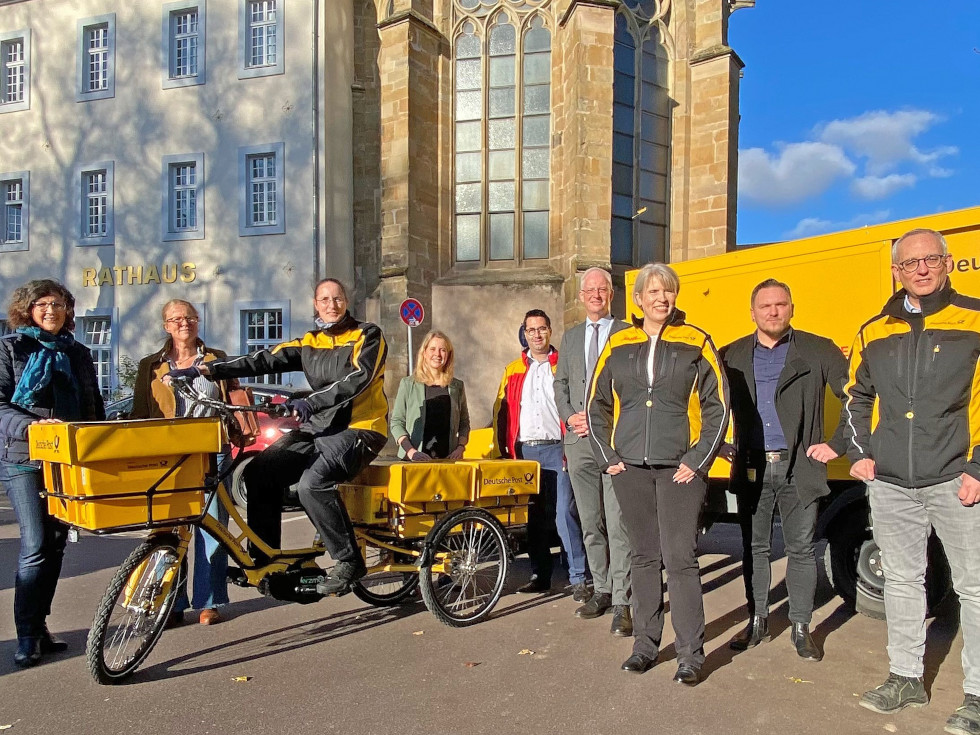 Die Deutsche Post DHL hat unter anderem E-Trikes und Elektro-Lastwagen im Einsatz. Vor dem Trierer Rathaus präsentieren Tanja Lauer (ver.di), Julia Hollweg (Klimaschutzmanagerin Stadt Trier), Zustellerin Katja Rößel, MdB Verena Hubertz, Thomas Schneider (Post-Betriebschef), OB Wolfram Leibe, Niederlassungsleiterin Anke Podewin, Sylvester Swierczynski (Betriebsratsvorsitzender) und Matthias Petersmarck (Zustellungsleiter für Trier) die umweltfreundlichen Fahrzeuge. Bild: Presseamt Trier
