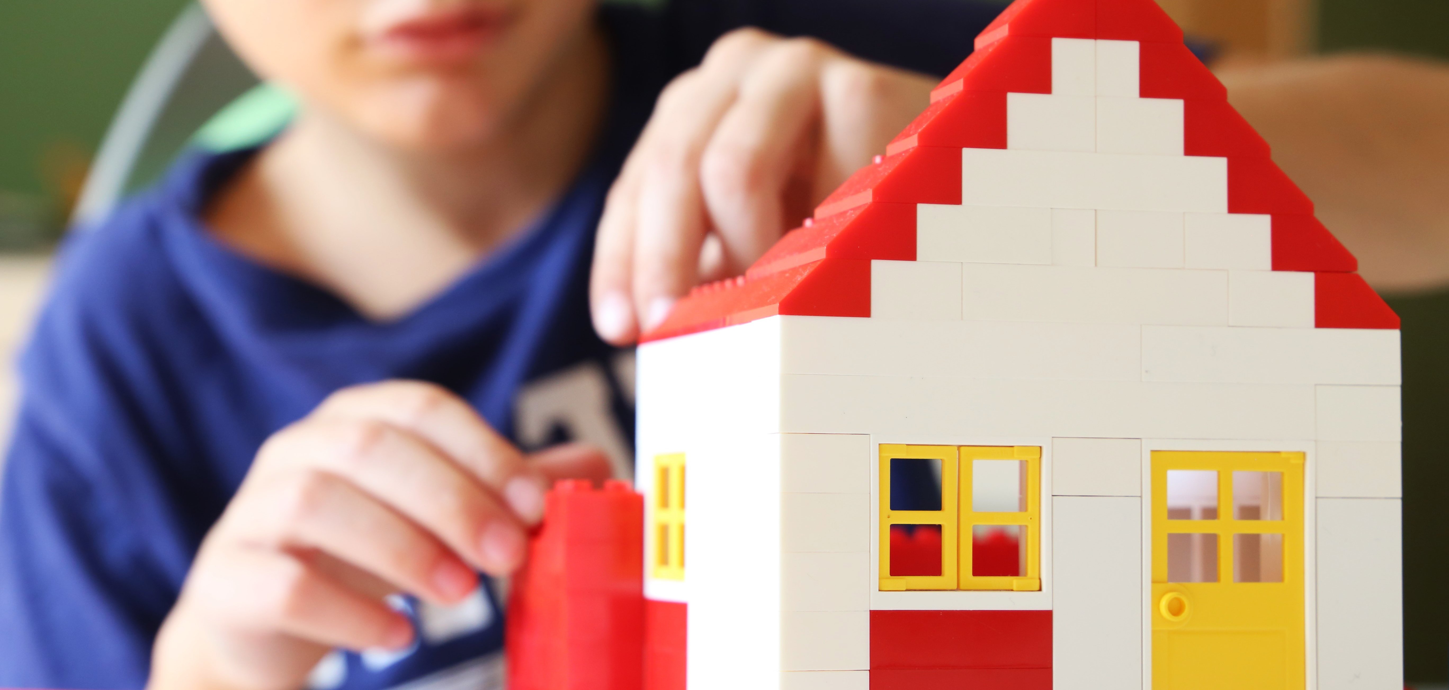 Das Foto zeigt einen Jungen, der mit Bausteinen ein Haus baut.
