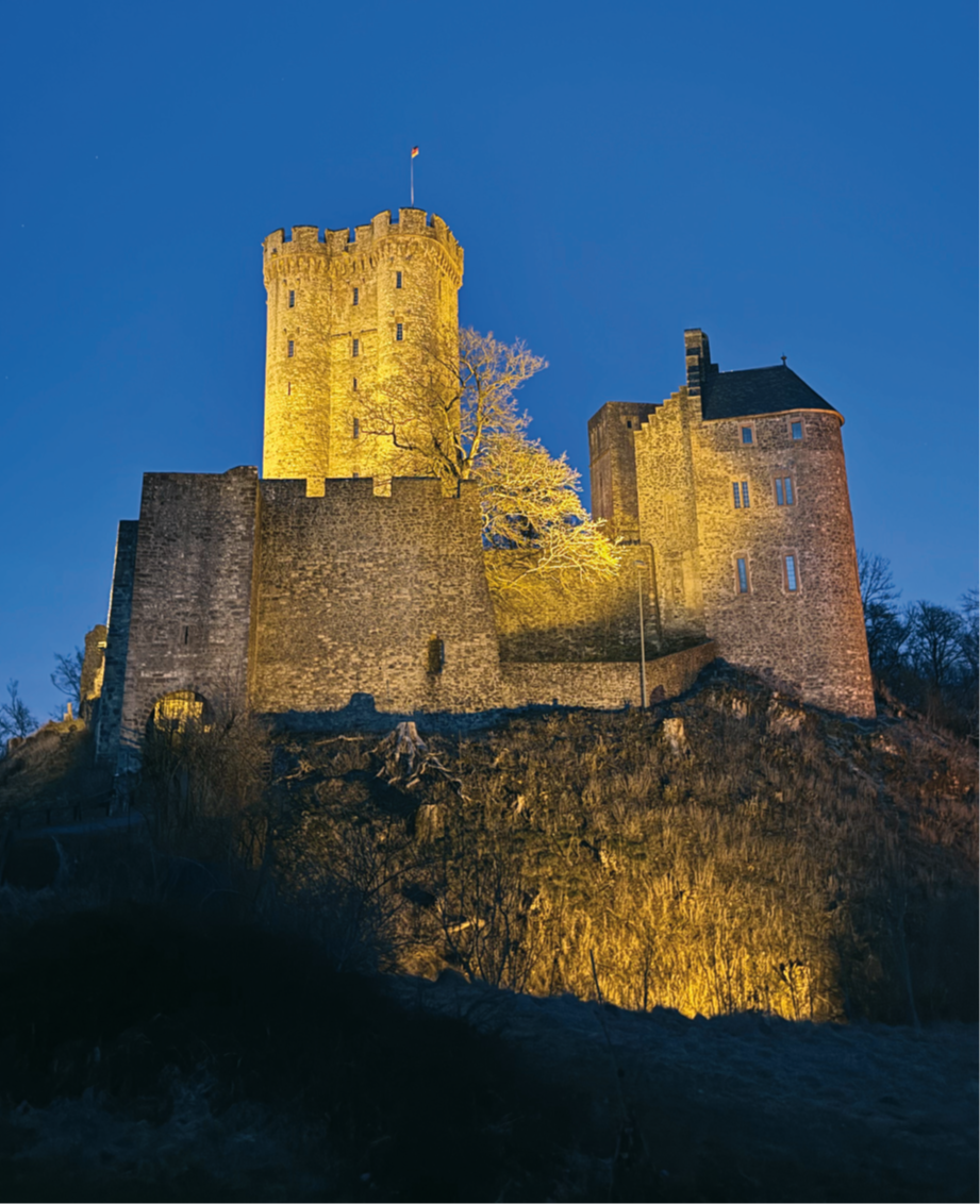 Angeleuchtete Burg auf einem Felsen bei Nacht.