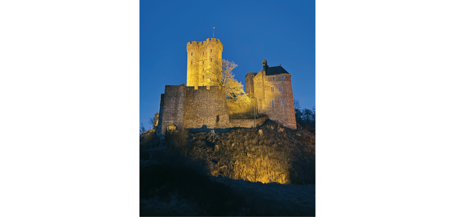 Angeleuchtete Burg auf einem Felsen bei Nacht.