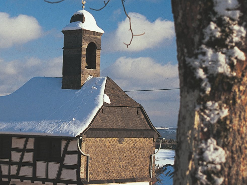 Das 1762 erbaute Glockenhaus prägt den Hattgensteiner Ortskern. Ursprünglich Wohnhaus des Gemeindedieners und Schulhaus, wird es seit 1975 als kleine Kirche genutzt. / Foto: Bruno L. Klamm, Mannheim