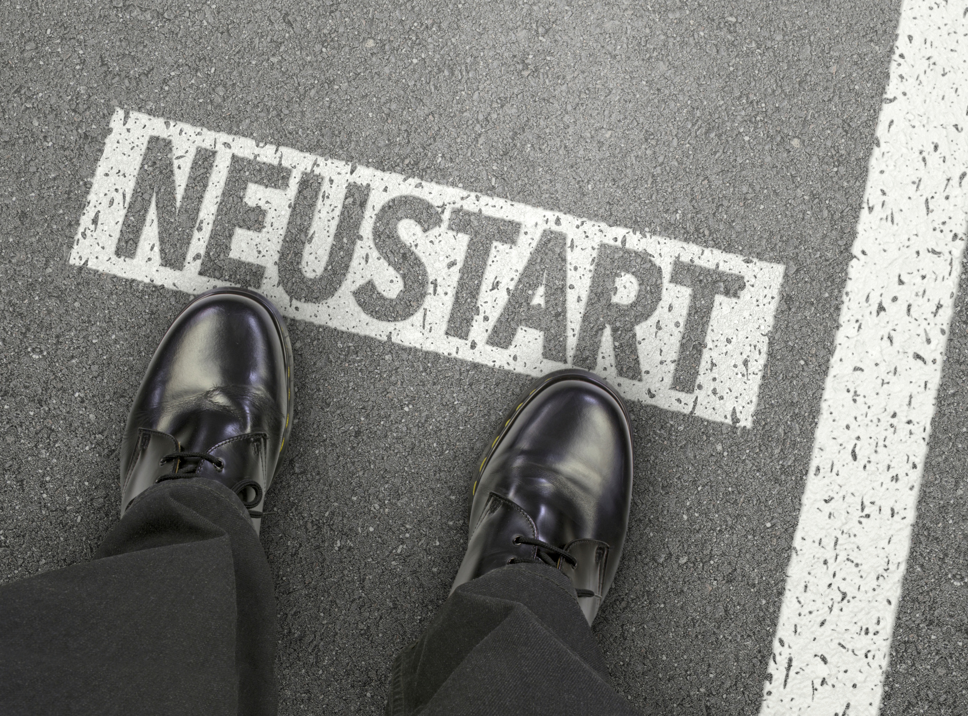 Füße auf einer Straße, auf der das Wort "Neustart" steht.