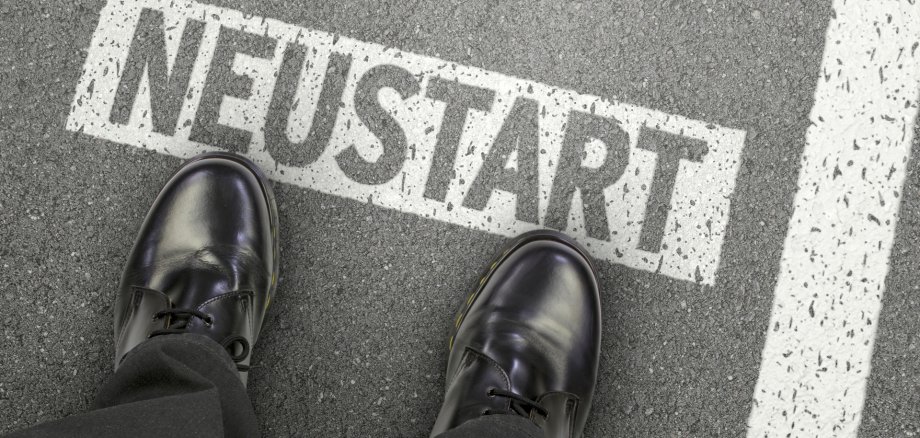 Füße auf einer Straße, auf der das Wort "Neustart" steht. 