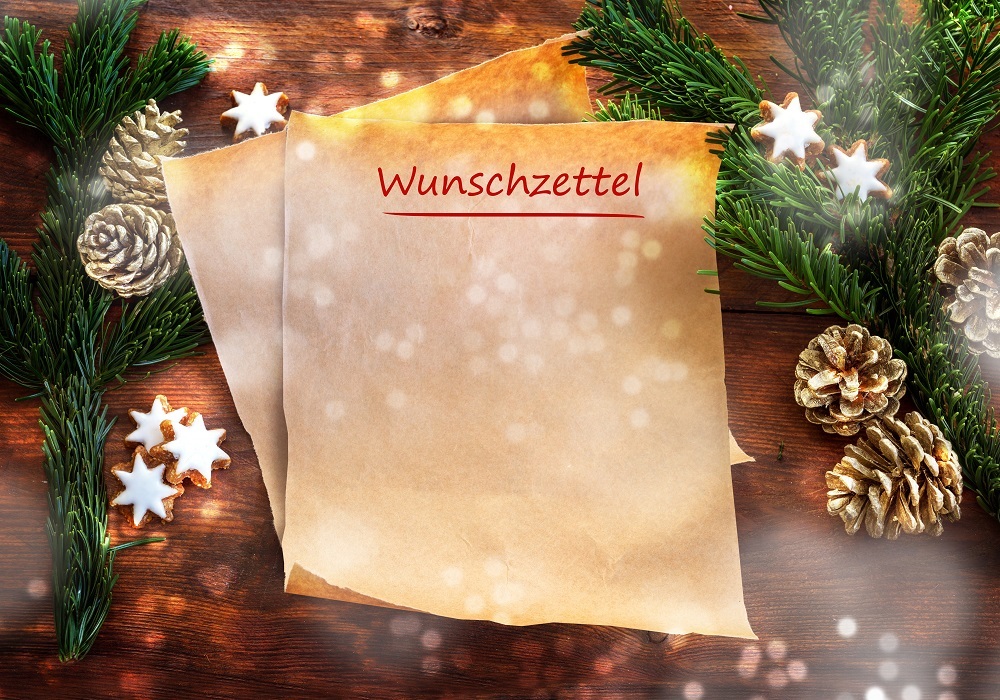 Paper sheet with german text Wunschzettel, that means wish list, between fir branches, cinnamon stars and Christmas decoration on rustic dark wood, copy space, top view from above