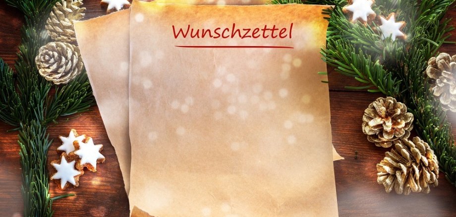 Paper sheet with german text Wunschzettel, that means wish list, between fir branches, cinnamon stars and Christmas decoration on rustic dark wood, copy space, top view from above