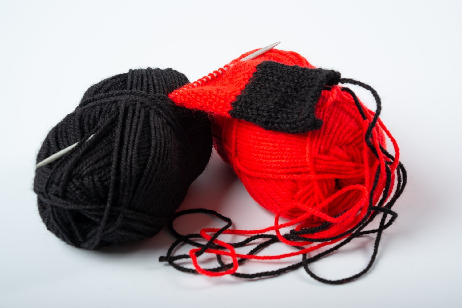 Ein schwarzes und ein rotes Wollknäuel liegen nebeneinander
