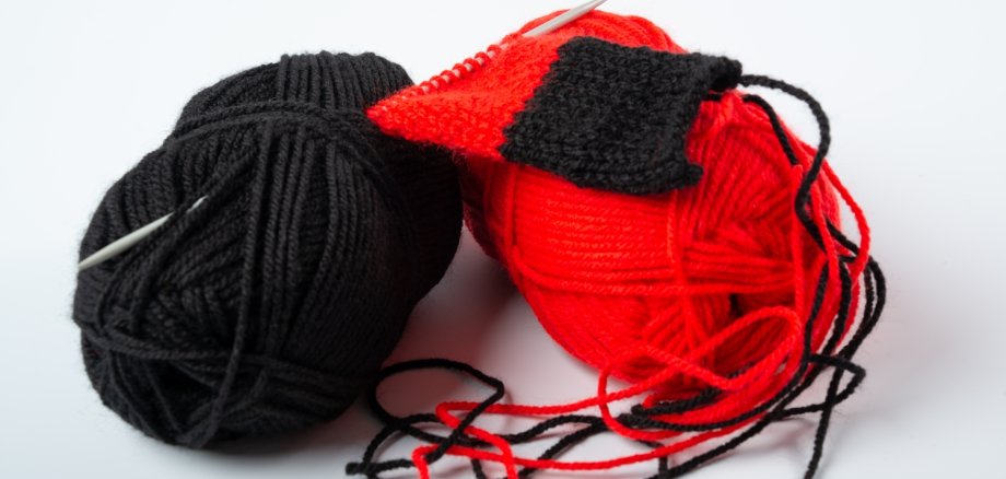 Ein schwarzes und ein rotes Wollknäuel liegen nebeneinander