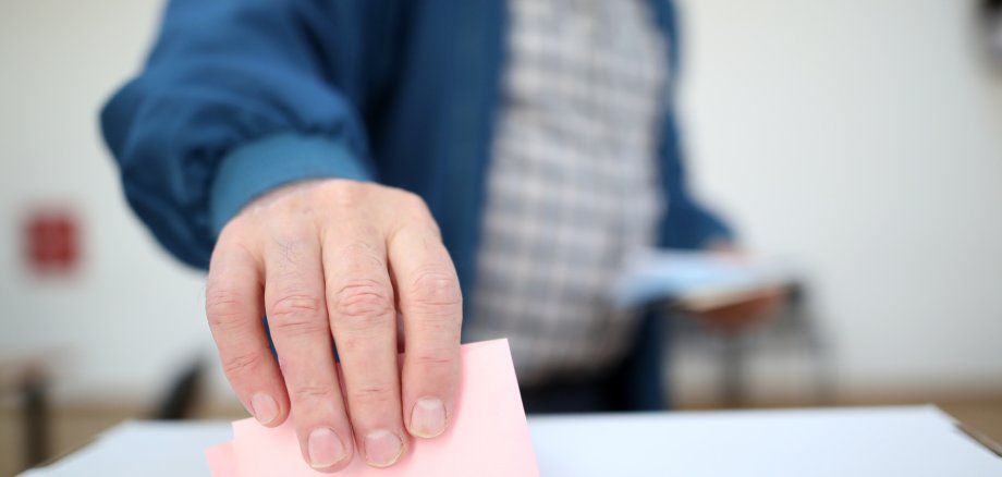 Mann wirft seinen Wahlschein in eine Wahlurne ein.
