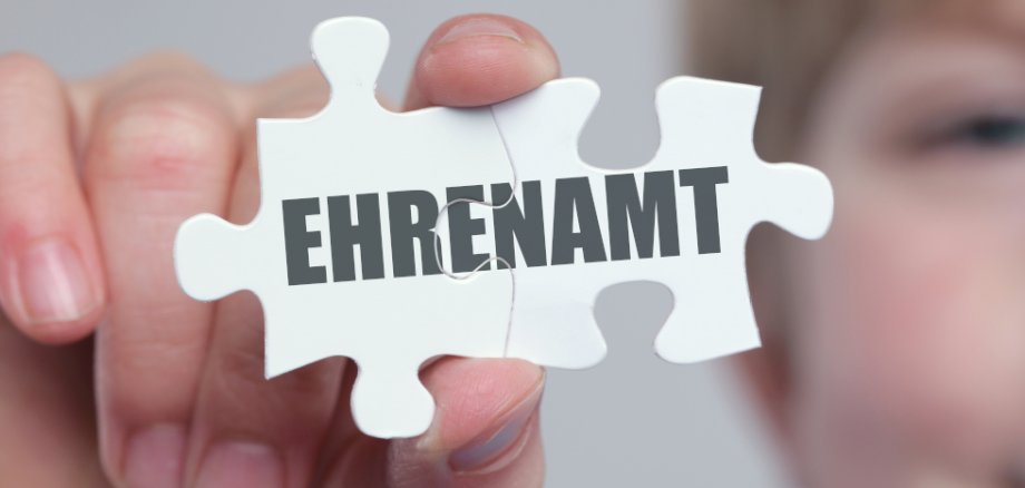 Ein Kind hält ein Puzzleteil in den Vordergrund mit der Aufschrift "Ehrenamt". 