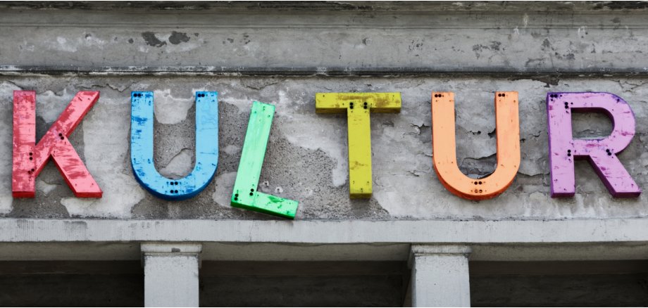 Bunter Schriftzug "Kutur" an einer grauen und brökelnden Hausfassade.