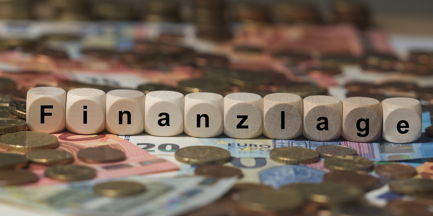 Euroscheine und Münzen. Darauf Würfel mit der Aufschrift "Finanzlage"