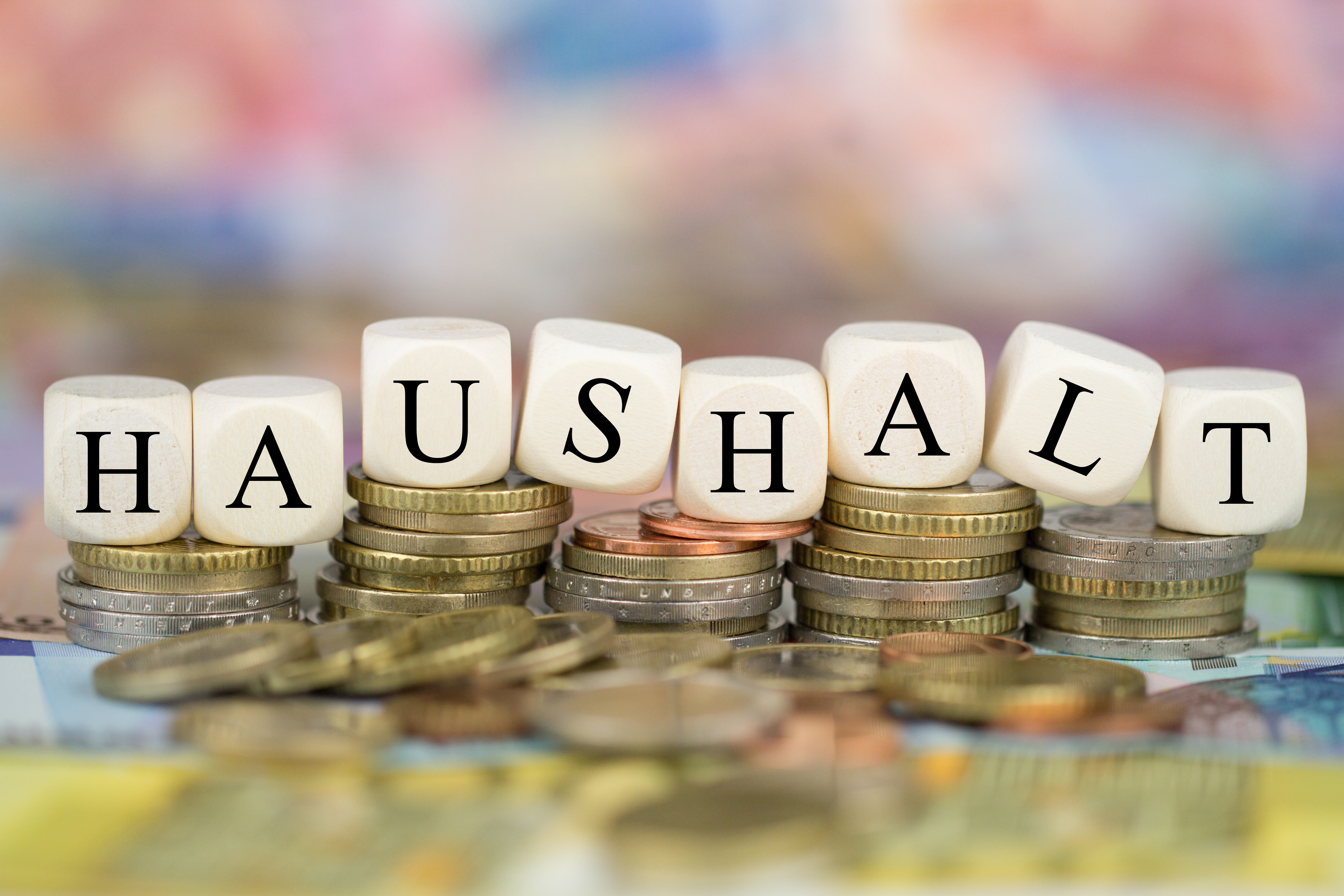 Das Bild zeigt gestapelte Euromünzen und Würfel mit der Aufschrift "Haushalt".