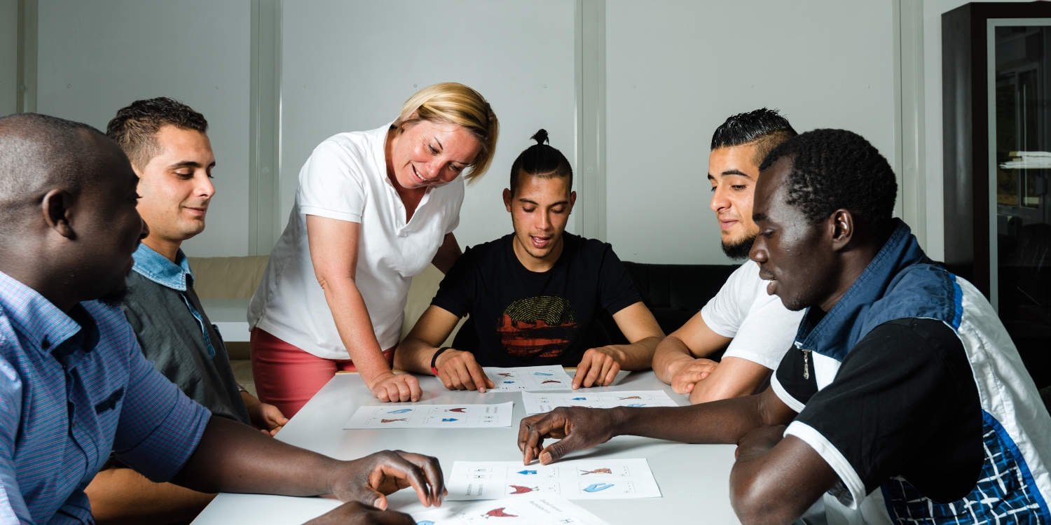 Männer und Lehrerin an einem Tisch mit Unterrichtunterlagen