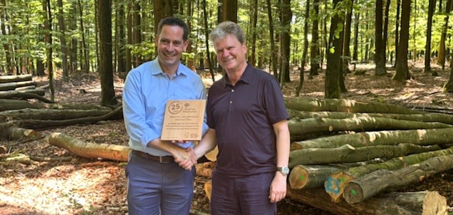 Moritz Petry, Geschäftsführendes Vorstandsmitglied des GStB, und Alfred Schumm, Geschäftsführer von FSC Deutschland. Moritz Petry, Geschäftsführendes Vorstandsmitglied des GStB, und Alfred Schumm, Geschäftsführer von FSC Deutschland, mit Urkunde vor einem Holzstapel im Wald.