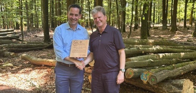 Moritz Petry, Geschäftsführendes Vorstandsmitglied des GStB, und Alfred Schumm, Geschäftsführer von FSC Deutschland. Moritz Petry, Geschäftsführendes Vorstandsmitglied des GStB, und Alfred Schumm, Geschäftsführer von FSC Deutschland, mit Urkunde vor einem Holzstapel im Wald.
