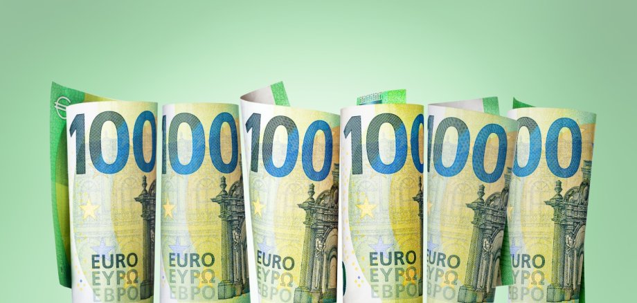 Gerollte Hundert-Euro-Scheine stehen senkrecht vor grünem Hintergrund.