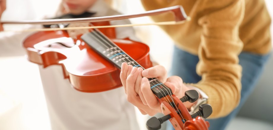 Musikleherin gibt kleinem Mädchen Geigenunterricht