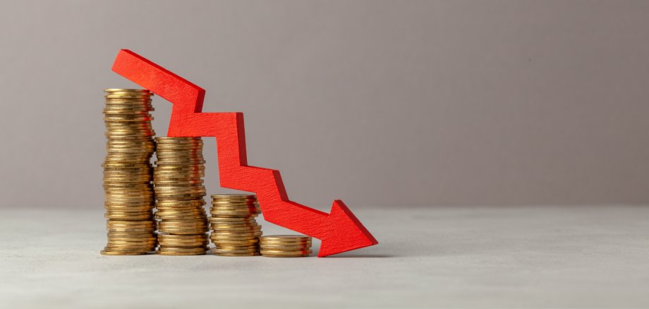 Green arrow down over stack of coins by ladder on gray background. Copy space for text.