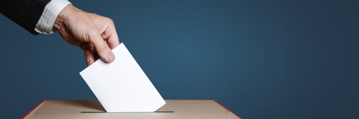 Hand wirft Stimmzettel in Wahlurne. 