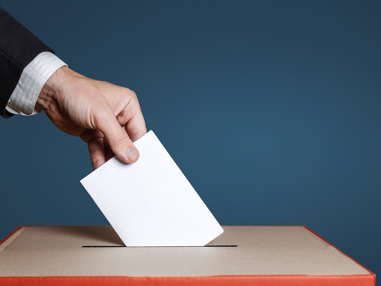 Hand wirft Stimmzettel in Wahlurne. 