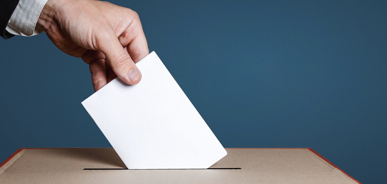 Hand wirft Stimmzettel in Wahlurne. 