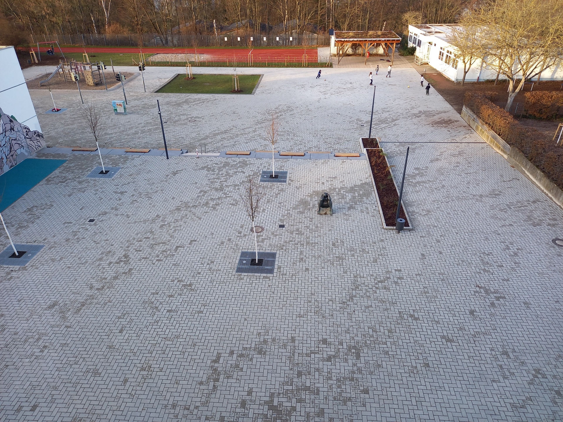 Der neue nachhaltige Schulhof der Woogbachschule in Speyer. Gepflasterter Schulhof mit neu gepflanzten Bäumen, Grünflächen sowie einem Spiel- und einem Sportplatz.