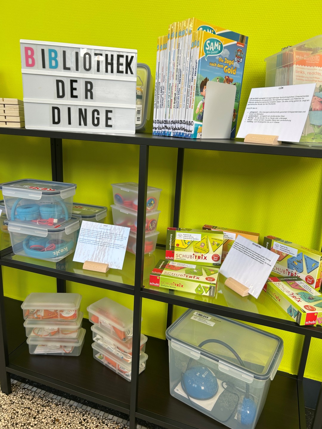 In einem Regal stehen Bücher, Spiele und mehrere mit Dingen gefüllte Kisten.