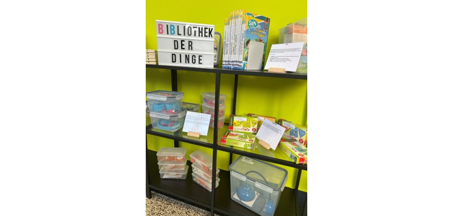 In einem Regal stehen Bücher, Spiele und mehrere mit Dingen gefüllte Kisten.