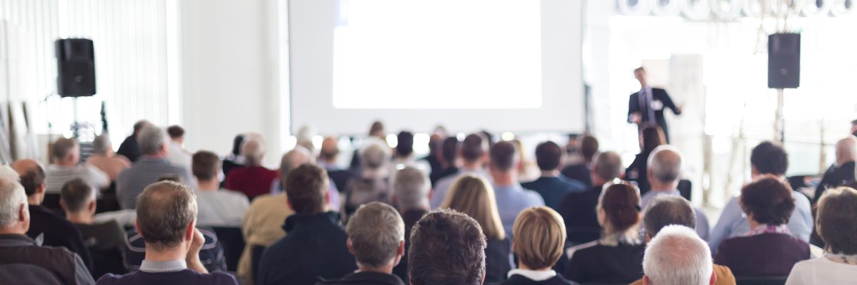 Personen schauen Redner auf Bühne zu